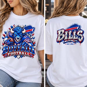 Puede incluir: Una camiseta blanca con un gráfico en la parte delantera y trasera. El frente muestra una mascota de búfalo azul con uniforme de fútbol americano y el texto BUFFALO FOOTBALL. La parte posterior muestra la palabra BILLS en letras metálicas con EST 1960.