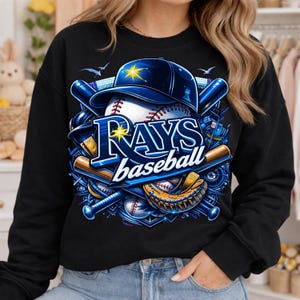 May include: Black sweatshirt featuring a baseball-themed graphic. The design includes a baseball, a blue baseball cap, bats, and a catcher's mitt. The text "RAYS baseball" is prominently displayed in blue and white.