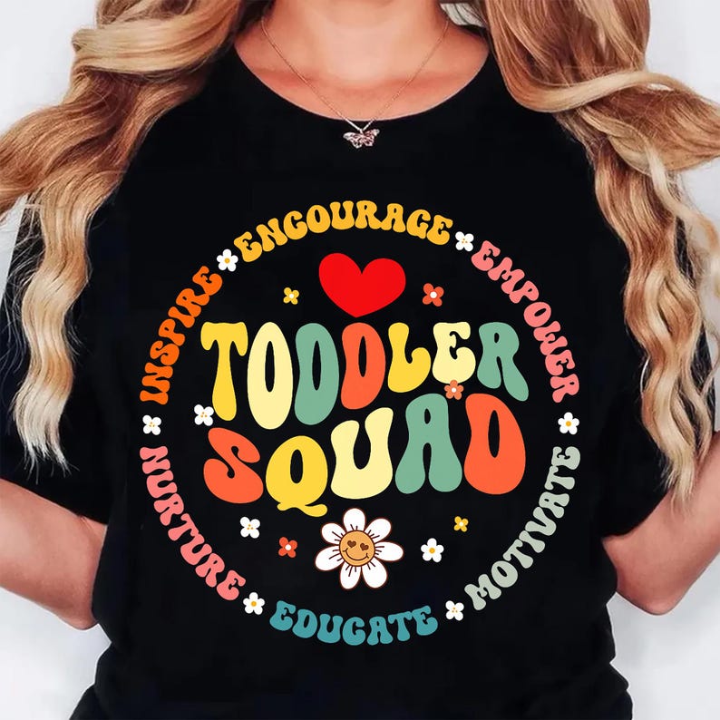 May include: Black t-shirt with a colorful graphic that says "Toddler Squad" in a retro font. The design includes a red heart, flowers, and the words "Inspire, Encourage, Empower, Motivate, Educate, Nurture".