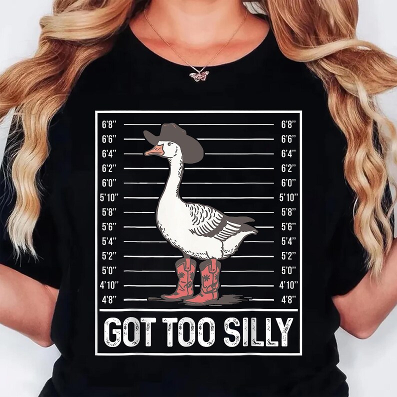 Może przedstawiać: Czarny t-shirt z kresk&oacute;wkową gęsią w kapeluszu i butach kowbojskich, na tle wykresu wzrostu. Gęś ma białe pi&oacute;ra i szare skrzydła. Tekst "GOT TOO SILLY" jest wyświetlany poniżej.