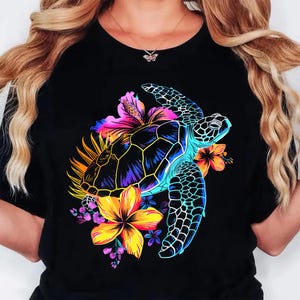 May include: Black t-shirt featuring a vibrant graphic of a sea turtle with a colorful floral arrangement. The turtle is depicted with a blue, yellow, and purple shell, surrounded by bright flowers in shades of pink, orange, and yellow.