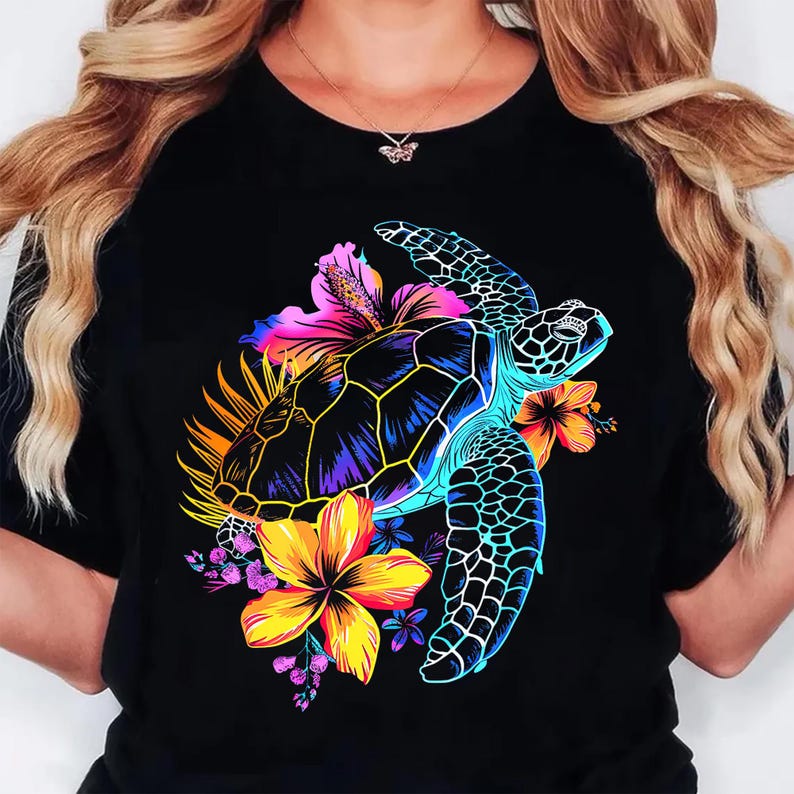 May include: Black t-shirt featuring a vibrant graphic of a sea turtle with a colorful floral arrangement. The turtle is depicted with a blue, yellow, and purple shell, surrounded by bright flowers in shades of pink, orange, and yellow.