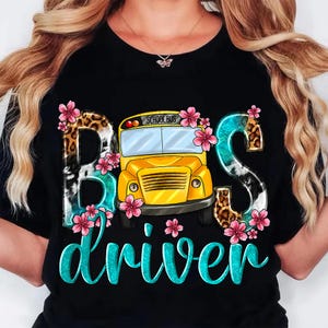 May include: Black t-shirt with a graphic design featuring the words "Bus driver" in turquoise script. The word "Bus" is stylized with animal print and floral accents, and a yellow school bus is in the center.