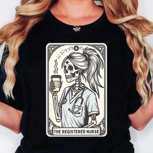 Pu&ograve; includere: T-shirt nero con grafica di un'infermiera scheletro che tiene una tazza di caff&egrave;, con uno stetoscopio e la scritta "THE REGISTERED NURSE". Il disegno &egrave; incorniciato in un bordo decorativo.