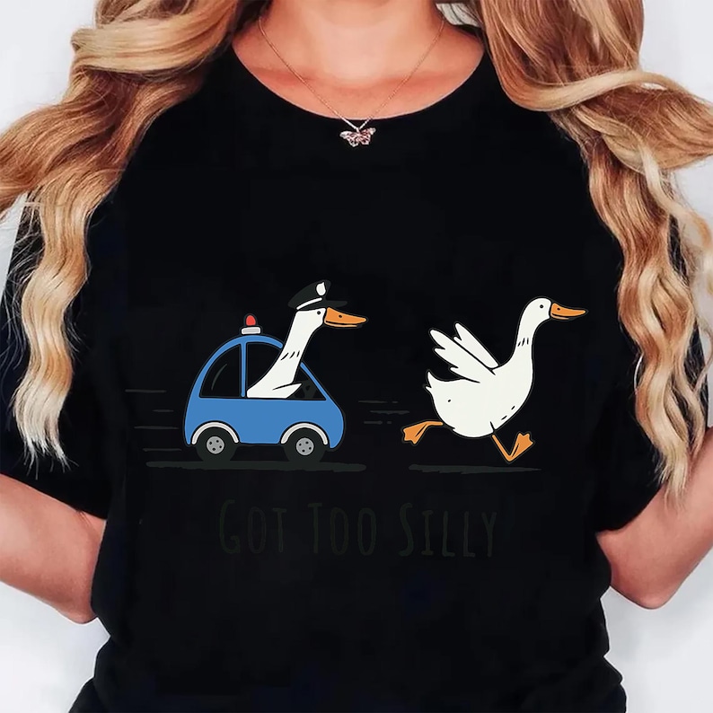 Może przedstawiać: Czarny t-shirt z zabawną grafiką gęsi w radiowozie goniącej inną gęś. Gęś w samochodzie ma na sobie czapkę policyjną. Pod ilustracją wydrukowano napis "GOT TOO SILLY".