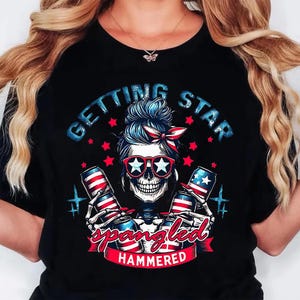 May include: Black t-shirt with a skull graphic wearing star-shaped sunglasses and a red, white, and blue bandana. The shirt features the text "GETTING STAR SPANGLED HAMMERED" with images of beer cans.