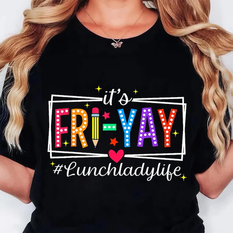 K&ouml;nnte beinhalten: Schwarzes T-Shirt mit dem Text "it's FRI-YAY" in bunten Buchstaben, einer Bleistiftgrafik und dem Hashtag "#Lunchladylife". Das Design beinhaltet einen wei&szlig;en rechteckigen Rahmen, Sterne und ein Herz.
