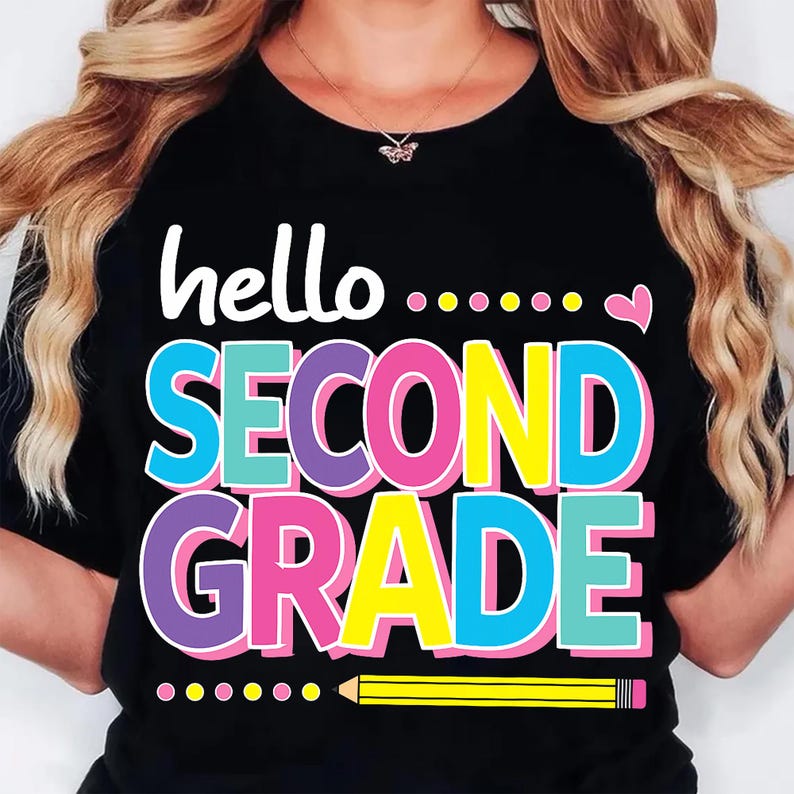 May include: A black t-shirt featuring the white text hello followed by colorful dots and a small pink heart. Below, the words SECOND GRADE are printed in large, bold, multi-colored letters. A yellow pencil graphic sits at the bottom of the design.