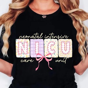 May include: Black t-shirt with the words "neonatal intensive NICU care unit" in a whimsical font. The letters NICU are in colorful, patterned blocks with a pink bow. A necklace with a butterfly pendant is visible.