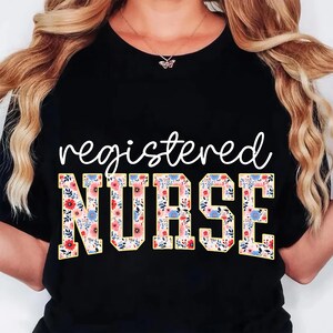 Pu&ograve; includere: T-shirt nero con le parole "registered NURSE" in corsivo bianco e lettere a blocchi floreali. Il design floreale comprende fiori rosa, blu e gialli su sfondo crema. La maglietta &egrave; a girocollo.