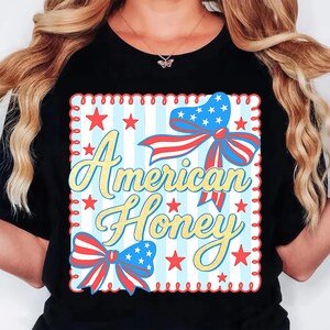 May include: Black t-shirt with a patriotic design. The design features the text "American Honey" in yellow script, surrounded by red stars and blue and red bows with white stars. The background has blue and white stripes.