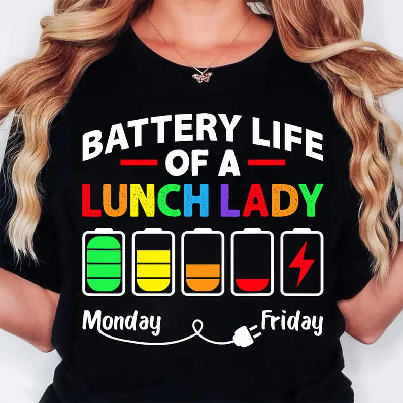 K&ouml;nnte beinhalten: Schwarzes T-Shirt mit dem Text "BATTERY LIFE OF A LUNCH LADY" in Wei&szlig; und bunten Buchstaben. Darunter befinden sich Akku-Symbole, die die Akkulaufzeit von Montag bis Freitag anzeigen. Unten ist eine Stecker-Grafik.