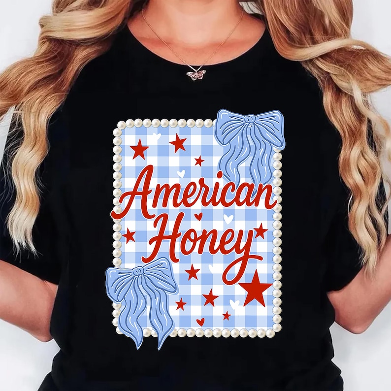 May include: Black t-shirt with a design that reads "American Honey" in red script. The design includes a blue and white gingham pattern, red stars, and blue bow accents, framed by a pearl border.