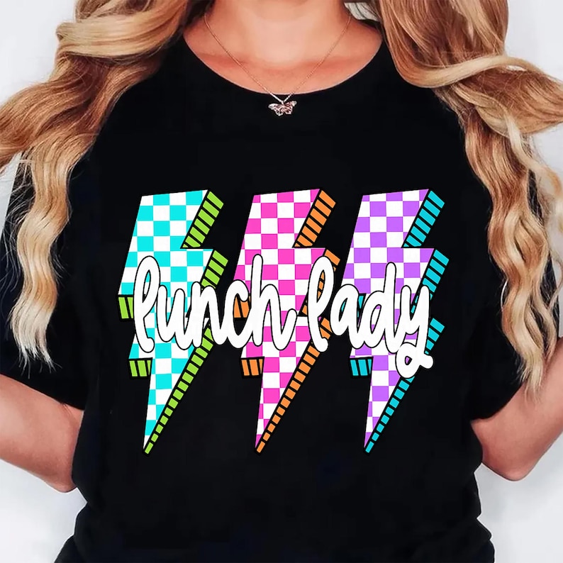 K&ouml;nnte beinhalten: Schwarzes T-Shirt mit drei Blitz-Grafiken in t&uuml;rkis, rosa und lila Karomustern. Die Worte "Lunch Lady" sind in wei&szlig;er Schrift &uuml;ber den Blitzen geschrieben.