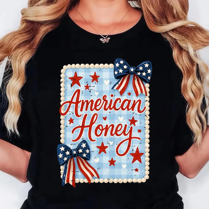 May include: Black t-shirt with a patriotic design. The design features the text "American Honey" in red script, set against a blue and white plaid background. Red stars and blue bows with white stars and red stripes complete the design.