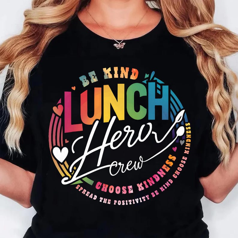 K&ouml;nnte beinhalten: Schwarzes T-Shirt mit einem farbenfrohen Grafikdesign. Das Design enth&auml;lt die Worte "BE KIND LUNCH Hero crew CHOOSE KINDNESS" in einem regenbogenfarbenen Kreis mit Herzen und einem Regenbogen. Der Satz "SPREAD THE POSITIVITY BE KIND" ist ebenfalls enthalten.
