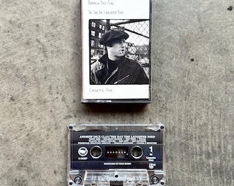 May include: A vintage cassette tape of Andrew Dice Clay's album "The Day The Laughter Died" with a black and white photo of the comedian. The clear cassette tape below displays the tracklist. The album is labeled "Cassette One".
