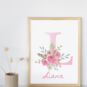 Könnte beinhalten: Gerahmter Druck mit einem rosa Buchstaben "L", verziert mit Aquarellblumen in Rosa und Grün. Der Name "Liana" ist darunter in Kursivschrift geschrieben. Das Kunstwerk befindet sich in einem hellen Holzrahmen.