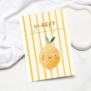 May include: A rectangular card with a yellow and white striped background. The card features a smiling cartoon lemon illustration with green leaves. The text "U-HEFT Liana Sophie" is written in a handwritten style.
