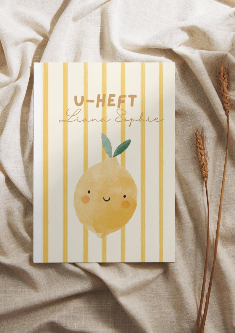 May include: A rectangular art print featuring a yellow lemon illustration with a smiling face and green leaves. The background has vertical yellow stripes. The text "U-HEFT Liana Sophie" is printed at the top. The print is on a beige fabric.