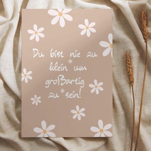May include: A beige card with white daisy illustrations and the German text "Du bist nie zu klein um großartig zu sein!" (You are never too small to be great!). Two stalks of wheat are on the right.