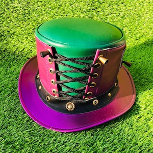 May include: A top hat featuring a green crown and a purple brim. The side of the hat includes a black lace-up corset detail with brass-toned eyelets and metal accents. A black band encircles the base of the crown, decorated with small brass studs.