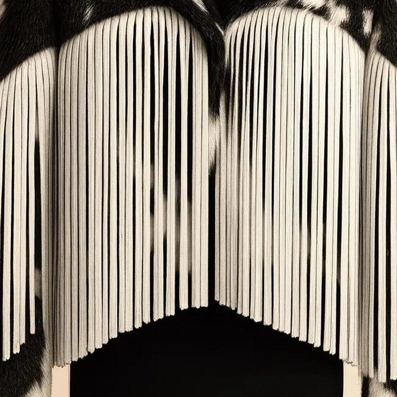 May include: Close-up of a black and white patterned textile with vertical white fringe. The fringe hangs in a curved shape, creating a layered effect. The textile has a zebra-like pattern.