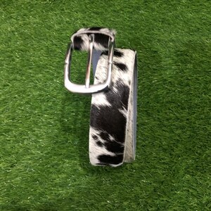 May include: A black and white cowhide belt with a silver-colored buckle. The belt is made of genuine leather and features a classic design. The belt is approximately 1.5 inches wide.
