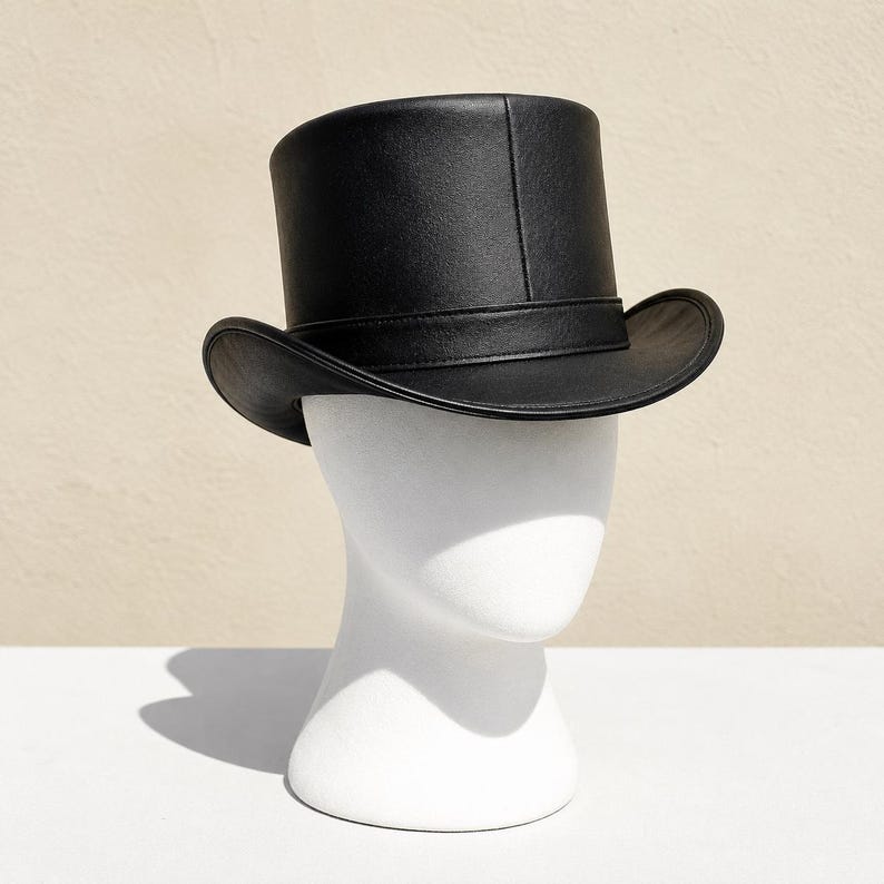 May include: A black top hat with a smooth, matte finish and a structured crown. The hat features a wide, slightly curved brim and a matching black band encircling the base of the crown, providing a clean and uniform appearance throughout.