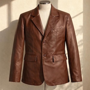 May include: A brown leather blazer with a classic two-button closure, notched lapels, and two front pockets. The jacket is displayed on a mannequin, showcasing its tailored fit and rich color.
