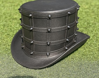 May include: A black leather top hat with a wide brim. The hat features a series of metal spikes around the crown and along the brim. Leather straps are arranged in a grid pattern around the hat.