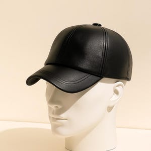 May include: A black leather baseball cap with a curved brim. The cap is displayed on a white mannequin head. The cap has a structured design with a small button on top.
