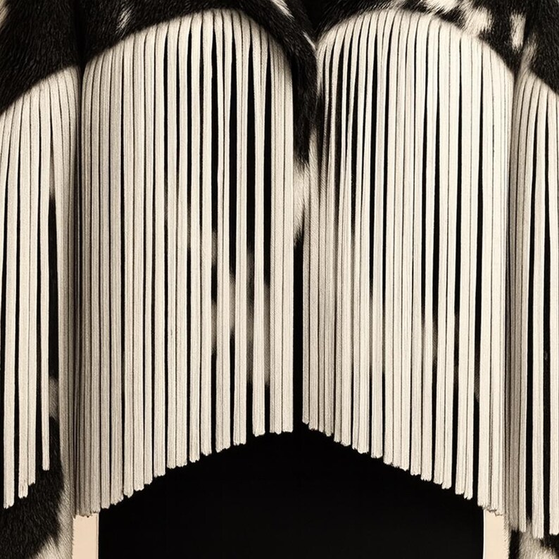 May include: A close-up of a black and white patterned textile. The design features vertical, cream-colored fringe-like elements against a black background. The top portion has a black and white spotted pattern, adding contrast to the overall design.