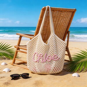 Op de afbeelding: Een cr&egrave;mekleurige gehaakte tote bag met een open mesh-ontwerp en twee schouderbanden. De voorkant van de tas toont de naam Chloe in verhoogde, lichtroze cursieve letters. De tas is gemaakt van zacht, getextureerd garen.