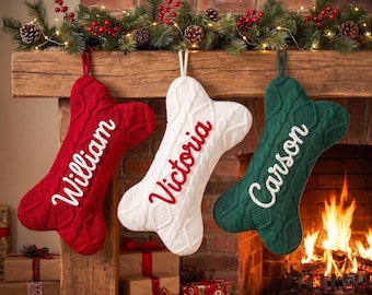 May include: Three bone-shaped Christmas stockings in red, white, and green with a cable knit texture. The red stocking features the name William in white, the white stocking features Victoria in red, and the green stocking features Carson in white.