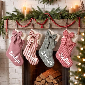 Op de afbeelding: Vier gepersonaliseerde kerstsokken hangend aan een houten schoorsteenmantel. Van links naar rechts tonen de sokken de namen Evelyn, Sarah, Daniel en Sophia in wit schrift, met patronen in effen roze, rode strepen, groen gingham en rood gingham.