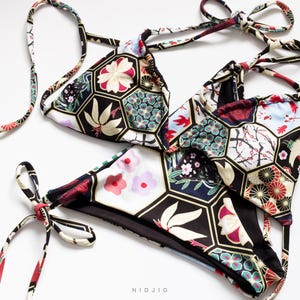 以下が含まれることがあります： 赤、白、青、緑、金色のミックスで幾何学模様が施された黒いビキニ。模様は日本の伝統的な芸術を思わせる。