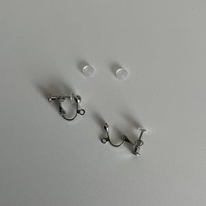 以下が含まれることがあります： 透明なプラスチック製のバックが付いた銀色のクリップ式イヤリング2つ。イヤリングはネジ式デザインです。