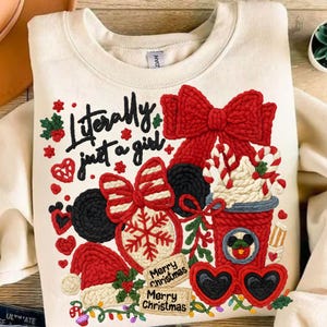 May include: Cream-colored sweatshirt with a festive Christmas design. Features a large red bow, Mickey Mouse ears, a Santa hat, and the text "Literally just a girl." Includes a coffee cup and heart-shaped sunglasses.