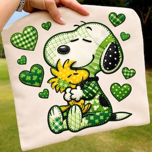 Könnte beinhalten: Ein cremefarbenes Kissenbezug mit einem Patchwork-Design von Snoopy, der Woodstock umarmt, umgeben von grünen Karomustern und gepunkteten Herzen. Snoopy und Woodstock sind hauptsächlich grün und gelb.