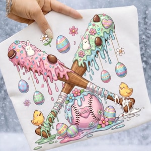 May include: A white t-shirt featuring a whimsical Easter-themed design. Two crossed baseball bats are decorated with dripping pastel-colored icing, chocolate candies, and bunny figures. A pink baseball with the word "EASTER" is also featured.