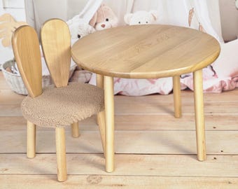 May include: A wooden children's table and chair set. The table is round and has a natural wood finish. The chair has bunny ears and a plush brown seat.