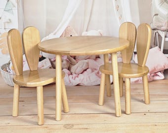 May include: A wooden children's table and two chairs with bunny ear backs. The table and chairs are a light natural wood color.