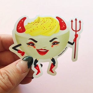 May include: A sticker of a devilish deviled egg with red horns, red lipstick, and a red pitchfork. The egg is wearing red boots and has a yellow yolk with red sprinkles. The sticker says "©Kellyportside 2018".