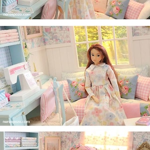 K&ouml;nnte beinhalten: Eine Miniatur-Puppenhaus-Szene mit einer Puppe in einem Blumenkleid, einer N&auml;hmaschine und einem B&uuml;cherregal mit Stoff. Der Raum ist in Pastellt&ouml;nen mit Blumtapeten und Kissen dekoriert. Nat&uuml;rliches Licht f&auml;llt durch ein Fenster.