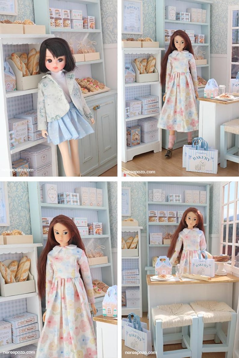 May include: A miniature bakery scene featuring two dolls in a detailed shop setting with shelves stocked with bread, boxes, and pastries. The shop includes a wooden table, stools, and a shopping bag labeled Bakery, all rendered in a light blue and white color palette.