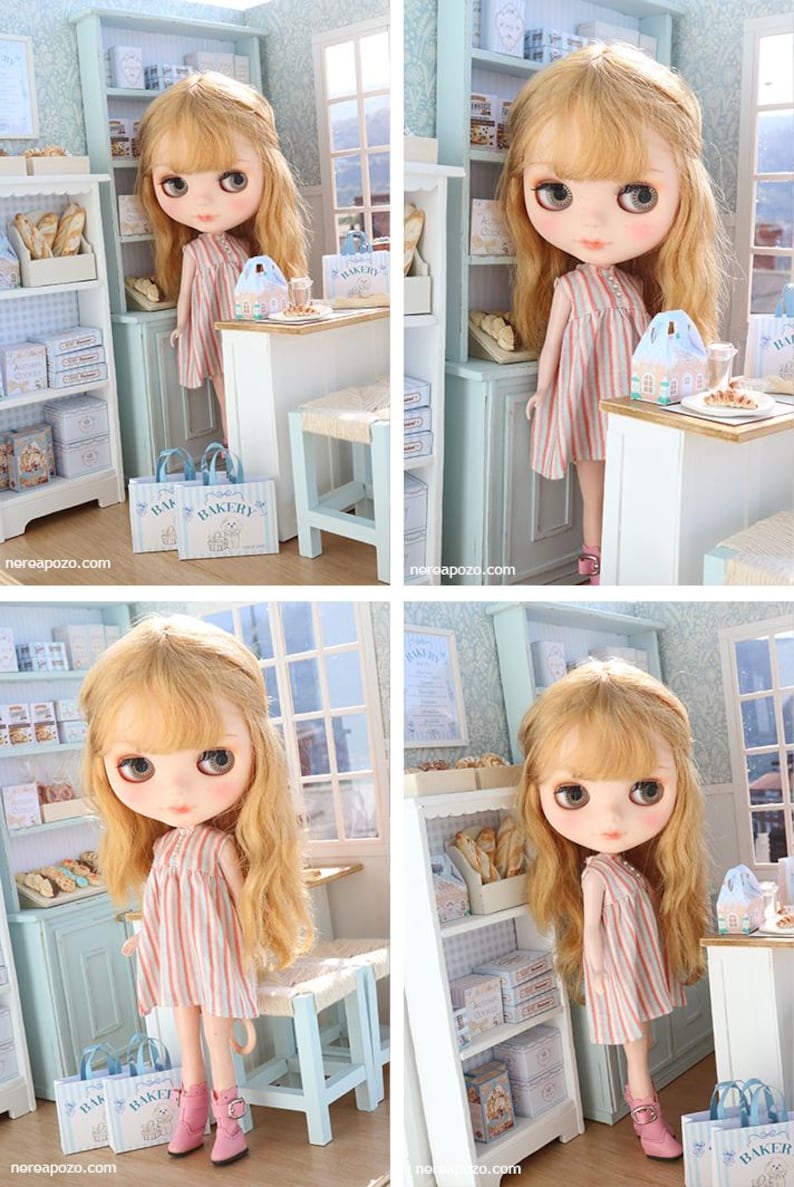 May include: A doll with long wavy blonde hair and large eyes wearing a sleeveless dress with vertical pink and white stripes and pink boots. The doll stands in a miniature bakery setting with light blue shelves, a counter, and paper bags.