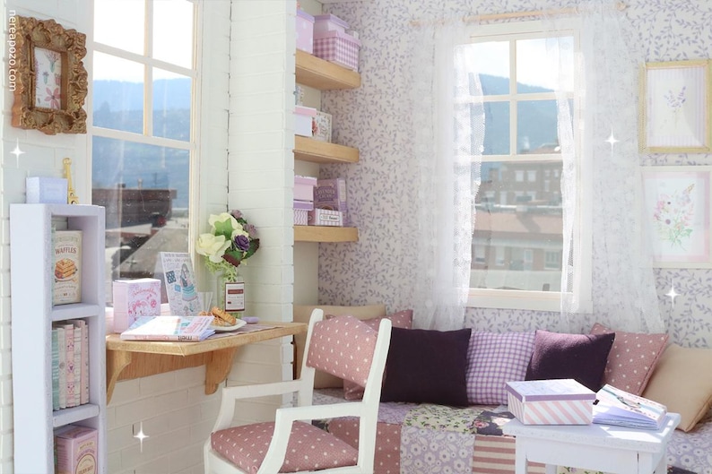 Pode incluir: Uma cena de quarto em miniatura com uma janela, secret&aacute;ria e &aacute;rea de estar. O quarto apresenta um esquema de cores branco e rosa, com papel de parede floral, prateleiras e caixas decorativas. Uma pequena mesa cont&eacute;m um livro e uma caixa de presente.