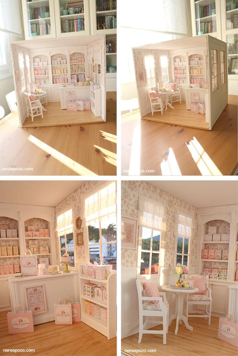 K&ouml;nnte beinhalten: Ein Miniatur-Puppenhaus-B&auml;ckereiladen mit wei&szlig;en Holzm&ouml;beln, einem runden Tisch mit zwei St&uuml;hlen, einer Verkaufstheke und Regalen voller kleiner Schachteln. Die W&auml;nde haben eine florale Tapete und der Laden enth&auml;lt Miniatur-Einkaufst&uuml;ten mit der Aufschrift Cake & Clover.