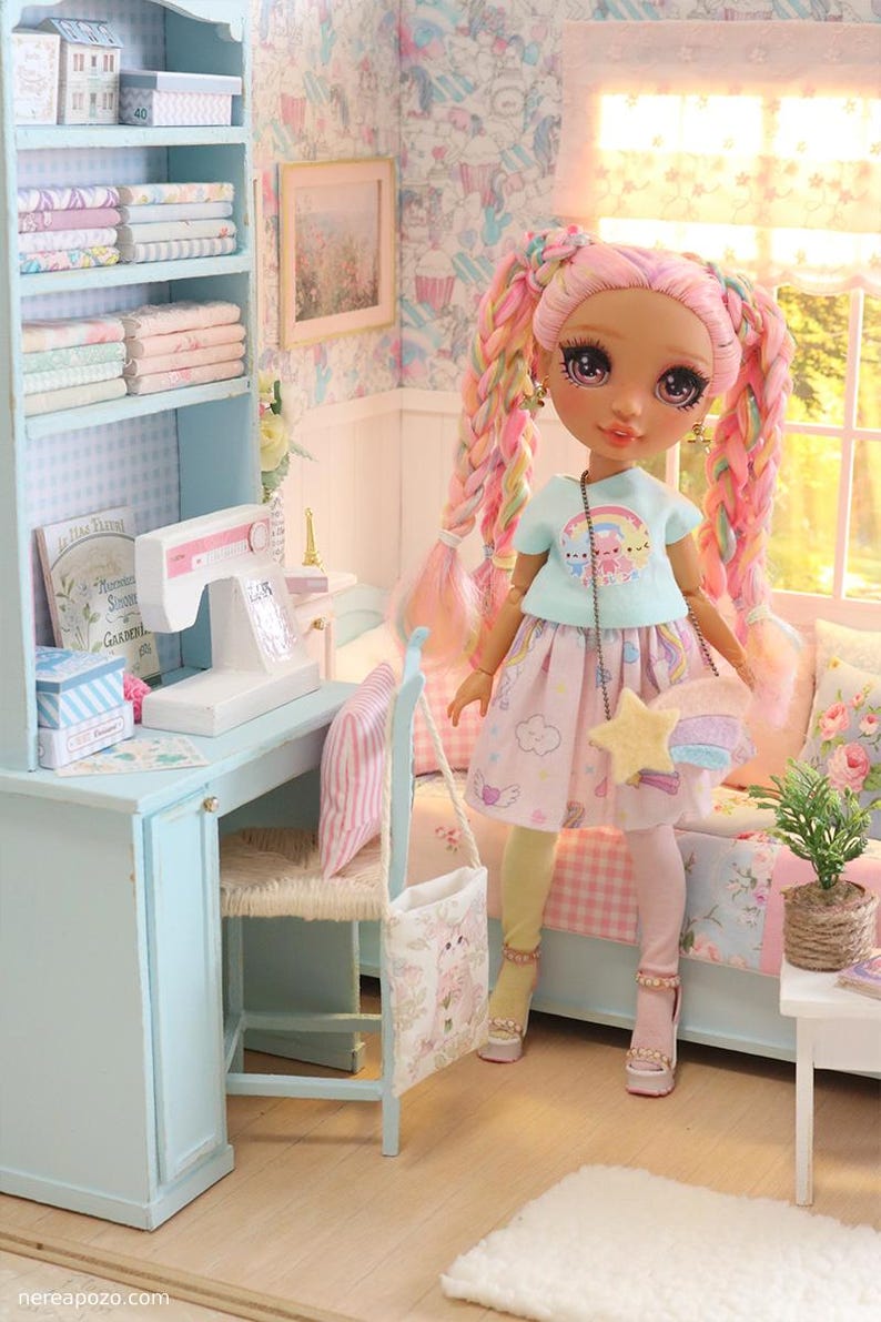 K&ouml;nnte beinhalten: Eine Puppe in einem pastellfarbenen Zimmer mit Schreibtisch, B&uuml;cherregal und Bett. Die Puppe hat rosa und Regenbogen-Z&ouml;pfe, tr&auml;gt ein hellblaues Oberteil, einen rosa Rock und eine sternf&ouml;rmige Handtasche. Der Raum ist mit floraler Tapete und Miniaturm&ouml;beln dekoriert.